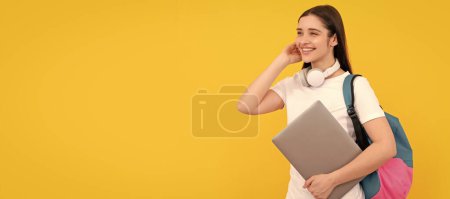 Foto de Cheerful young girl with backpack hold laptop in headphones on yellow background, e-learning. Woman isolated face portrait, banner with copy space - Imagen libre de derechos
