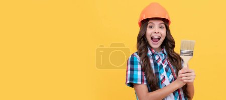 Renovation child, amazed kid with curly hair in construction helmet hold painting brush, renovator. Child builder in helmet horizontal poster design. Banner header, copy space