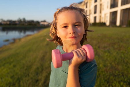 Photo for Kids sport training outdoor. Child boy pumping up biceps muscles with dumbbell. Fitness kids with dumbbells - Royalty Free Image