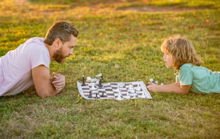 glückliche Familie von Eltern und Sohn spielen Schach auf grünem Gras im Park im Freien, Schachspiel.