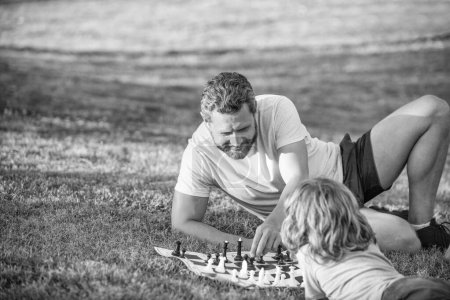Photo for Strategic and tactic. tutorship. dad and boy play logic game. father and son playing chess on grass in park. fathers day. family day. parenthood and childhood. checkmate. spending time together. - Royalty Free Image
