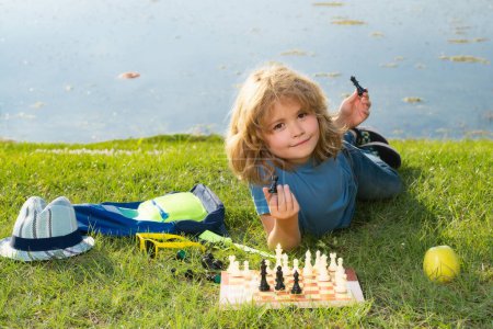 Photo for Kid shows chess pieces on a chessboard. Early development. Boy thinking about chess in summer park. The concept of learning and growing children. Outdoor game, kids hobby and lifestyle - Royalty Free Image
