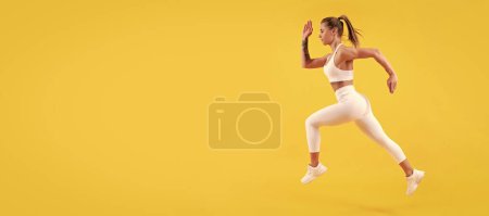 Foto de Enérgico corredor de fitness mujer corriendo sobre fondo amarillo. Mujer saltando corriendo banner con simulacro de copyspace - Imagen libre de derechos