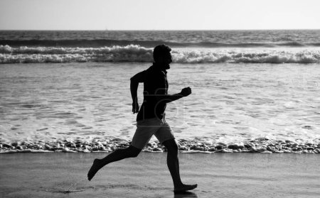Foto de Deportista correr rápido para ganar en el océano. actividad de entrenamiento matutino. hombre sano corriendo en la playa. verano enérgico. corredor sentir la libertad. Date prisa. resistencia y resistencia. silueta del velocista. - Imagen libre de derechos