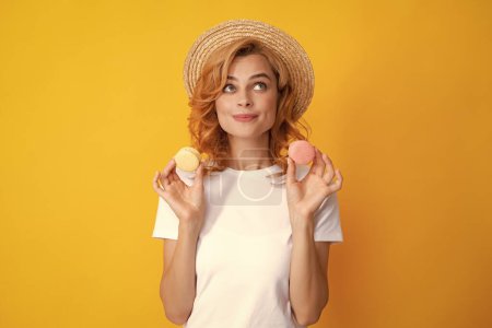 Téléchargez les photos : Jeune femme heureuse isolée sur fond jaune mangeant des macarons. Fille manger macarons français - en image libre de droit