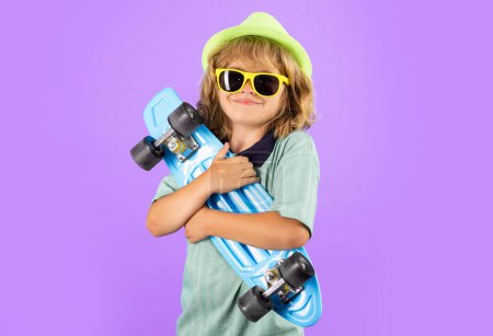 Photo for Fashion child in summer shirt stylish hat and sunglasses. Cute child with skateboard on color isoalted background. Funny kid boy, stylish skater holding skateboard in studio - Royalty Free Image