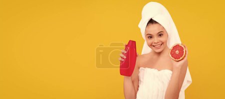 Photo for Smiling kid in towel with grapefruit shampoo bottle on yellow background. Cosmetics and skin care for teenager child, poster design. Beauty kid girl banner with copy space - Royalty Free Image