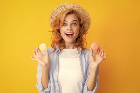 Téléchargez les photos : Jeune femme heureuse isolée sur fond jaune mangeant des macarons. Fille manger macarons français - en image libre de droit