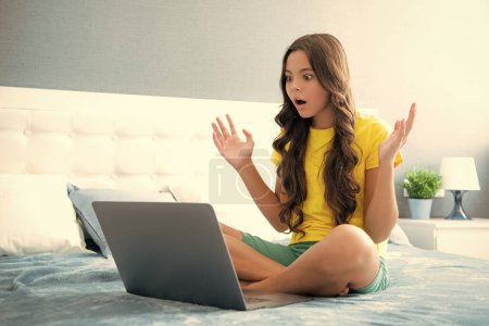 Adolescente estudiante de la escuela en casa en la cama con el ordenador portátil. Rostro sorprendido, emociones sorpresa de adolescente