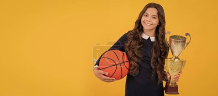 Photo for Happy teen girl hold basketball ball and champion cup on yellow background, champion. Horizontal poster of isolated child face, banner header, copy space - Royalty Free Image
