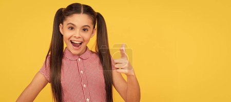 Téléchargez les photos : Happy girl child point finger gun hand gesture yellow background, pointing. Child face, horizontal poster, teenager girl isolated portrait, banner with copy space - en image libre de droit