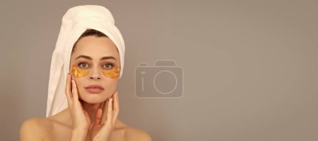 Téléchargez les photos : Eye patches, patch under eyes. beautiful girl with terry towel use facial golden eye patch for skin, healthy skin. Beautiful woman isolated face portrait, banner with mock up copy space - en image libre de droit