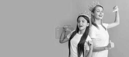 Photo for Mother and daughter child banner, copy space, isolated background. Happy woman and girl kid in crowns point fingers at promotional tshirts for copy space, advert - Royalty Free Image