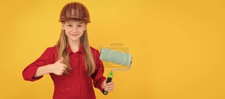 Photo for Renovation child, teen child smile in builder hard hat with paint roller on yellow wall. thumb up. Child builder in helmet horizontal poster design. Banner header, copy space - Royalty Free Image
