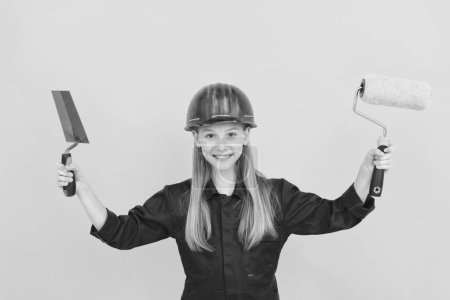 Photo for Happy teen child in builder hard hat with paint roller and spatula on yellow wall. - Royalty Free Image