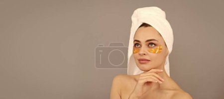 Foto de Sensual dama con toalla de rizo utilizar parche facial dorado ojo para la piel, hidrogel. Hermosa mujer aislado retrato de la cara, pancarta con espacio de copia simulada - Imagen libre de derechos