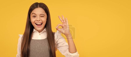 happy teen girl behind blank pink paper sheet for copy space ok gesture, announcement. Child face, horizontal poster, teenager girl isolated portrait, banner with copy space