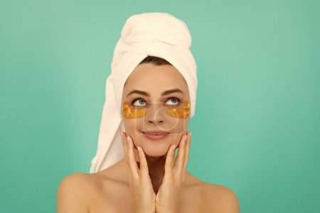young woman smile has collagen gold eye patches on face with towel.
