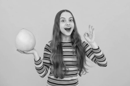 Foto de Funny teenage girl hold citrus fruit pummelo or pomelo, big green grapefruit isolated on yellow background. Excited face, cheerful emotions of teenager girl - Imagen libre de derechos