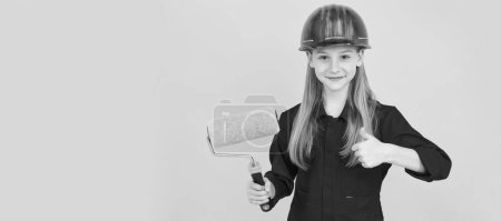 Renovation child, teen child smile in builder hard hat with paint roller on yellow wall. thumb up. Child builder in helmet horizontal poster design. Banner header, copy space