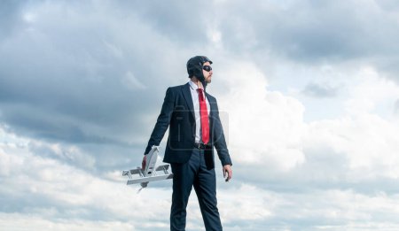 businessman in suit and pilot hat launch plane toy on sky background. promotion.