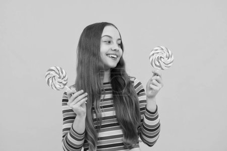 Foto de Teen girl hold lollipop caramel on yellow background, candy shop. Teenager with sweets suckers - Imagen libre de derechos