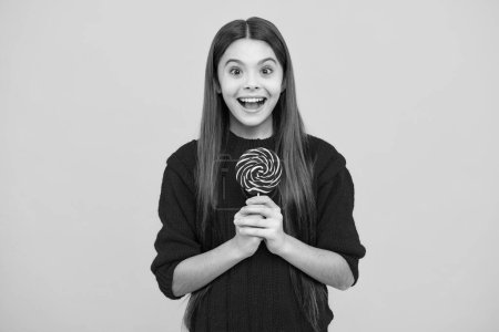 Foto de Funny child with lollipop over yellow isolated background. Sweet childhood life. Teen girl with yummy caramel lollipop, candy shop. Teenager with sweet sucker - Imagen libre de derechos