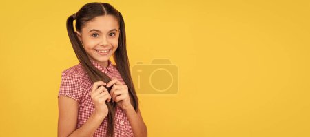 Schöne Mädchen Kind mit schüchternem Lächeln berühren Haare gelben Hintergrund. Kindergesicht, horizontales Poster, isoliertes Porträt eines Teenagers, Banner mit Kopierraum
