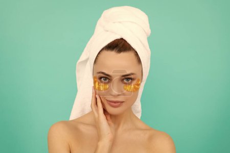 Foto de Chica joven tiene parches de colágeno ojo de oro en la cara con toalla. - Imagen libre de derechos