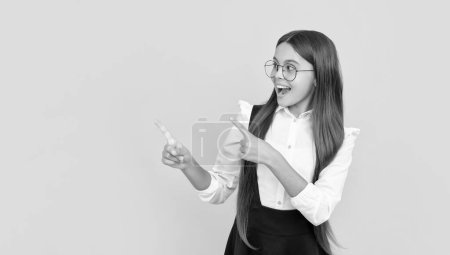 happy teen girl in school uniform and glasses for vision protection pointing finger on copy space, eyecare.