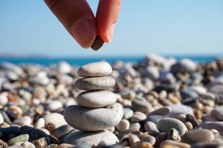 Téléchargez les photos : Équilibre d'esprit - abstrait - main mettant du caillou sur la tour de pierres sur la plage ensoleillée - en image libre de droit