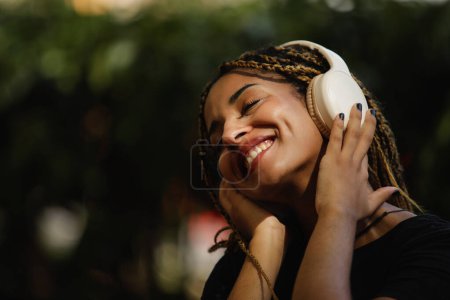 Foto de Mujer sonriente se relaja mientras disfruta y escucha algo de música con auriculares en el parque - Imagen libre de derechos