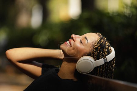 Foto de Mujer joven y relajada escuchando música con auriculares en el parque - Imagen libre de derechos