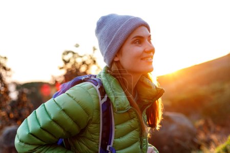 Foto de Retrato de una senderista caucásica sonriente vestida con ropa de invierno delante de un sendero de montaña por la mañana temprano - Imagen libre de derechos