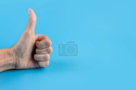 Hand with thumbs up on a blue background close up. Copy space.