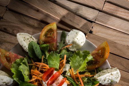Photo for Yummy salad with tomato, mozzarella, rocket, carrot, on a well presented plate on a wooden table - Royalty Free Image