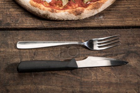 Photo for Slice of pizza with knife and fork resting on wooden table - Royalty Free Image