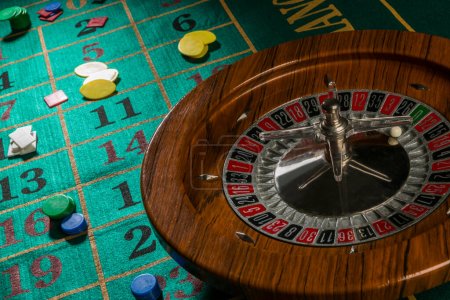 Téléchargez les photos : Roue de roulette en bois isolée sur une table de jeu verte avec des puces colorées - en image libre de droit