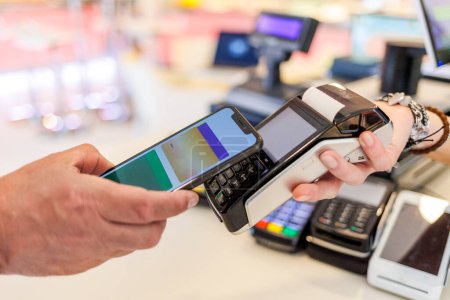 Téléchargez les photos : Détail du paiement par carte de crédit avec un smartphone vers les pos tenus par la main d'une vendeuse - en image libre de droit