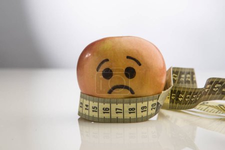 Téléchargez les photos : Une pomme avec un visage dessiné est enroulée autour d'un ruban à mesurer - en image libre de droit
