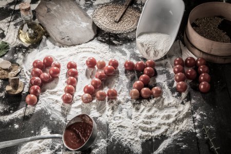Photo for Written "pizza" with cherry tomatoes on a table full of ingredients such as flour, tomato sauce, oil, mushrooms etc. - Royalty Free Image