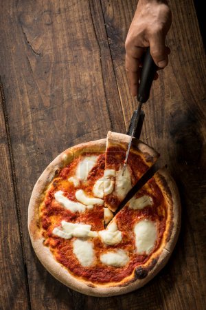 Photo for Pizza margherita cut with a wedge shot from above isolated on a wooden table - Royalty Free Image