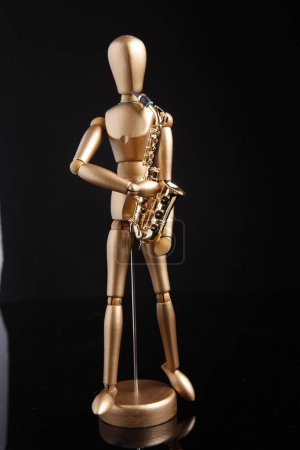 Téléchargez les photos : Cagliari, Italie - 12 janvier 2011 : Marionnette en bois joue un saxophone doré, isolé sur fond noir - en image libre de droit