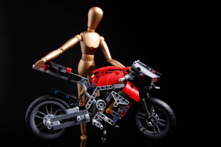 Téléchargez les photos : Cagliari, Italie - 12 janvier 2011 : Marionnette en bois porte une moto construite avec lego, isolée sur fond noir - en image libre de droit