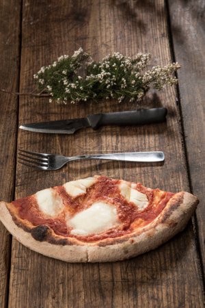 Photo for Slice of pizza with knife and fork resting on wooden table - Royalty Free Image