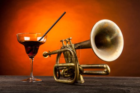 Photo for Brass trumpet on wooden table, orange background and glass with drink - Royalty Free Image