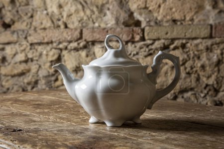 Photo for White teapot on wooden table and old brick wall background - Royalty Free Image