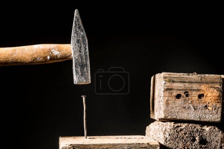 Photo for Hammer hits a nail inside a wooden board, isolated on a black background - Royalty Free Image