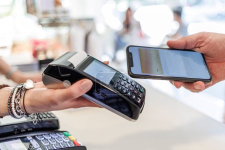 Foto de Detalle del pago con tarjeta de crédito con un smartphone hacia los pos en poder de la mano de una vendedora - Imagen libre de derechos