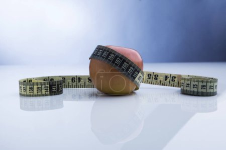Photo for Red apple wrapped in a tape measure isolated on a blue background - Royalty Free Image